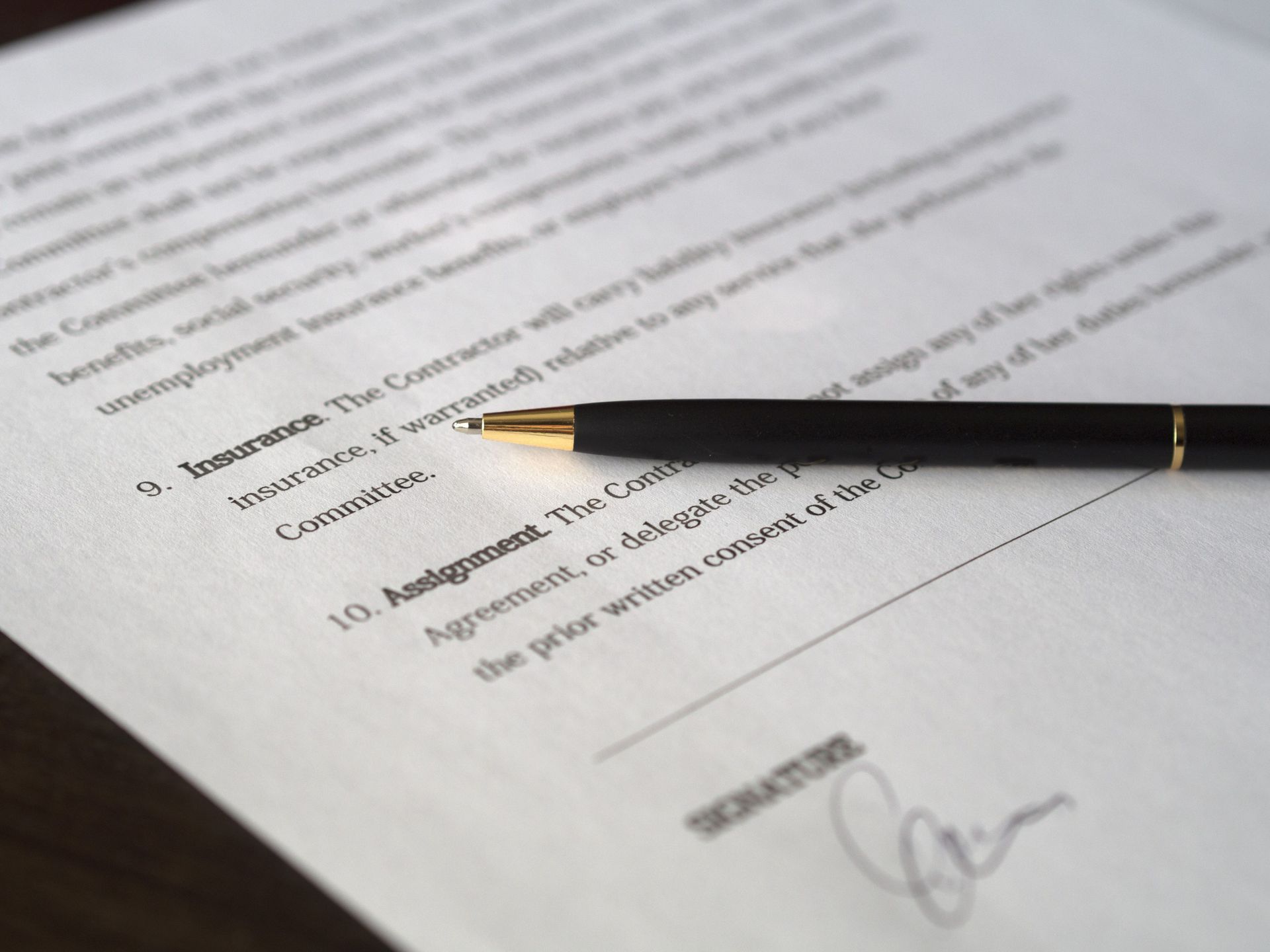 Hand filling out a paper bill beside a red notebook labeled “Pay” on a wooden desk