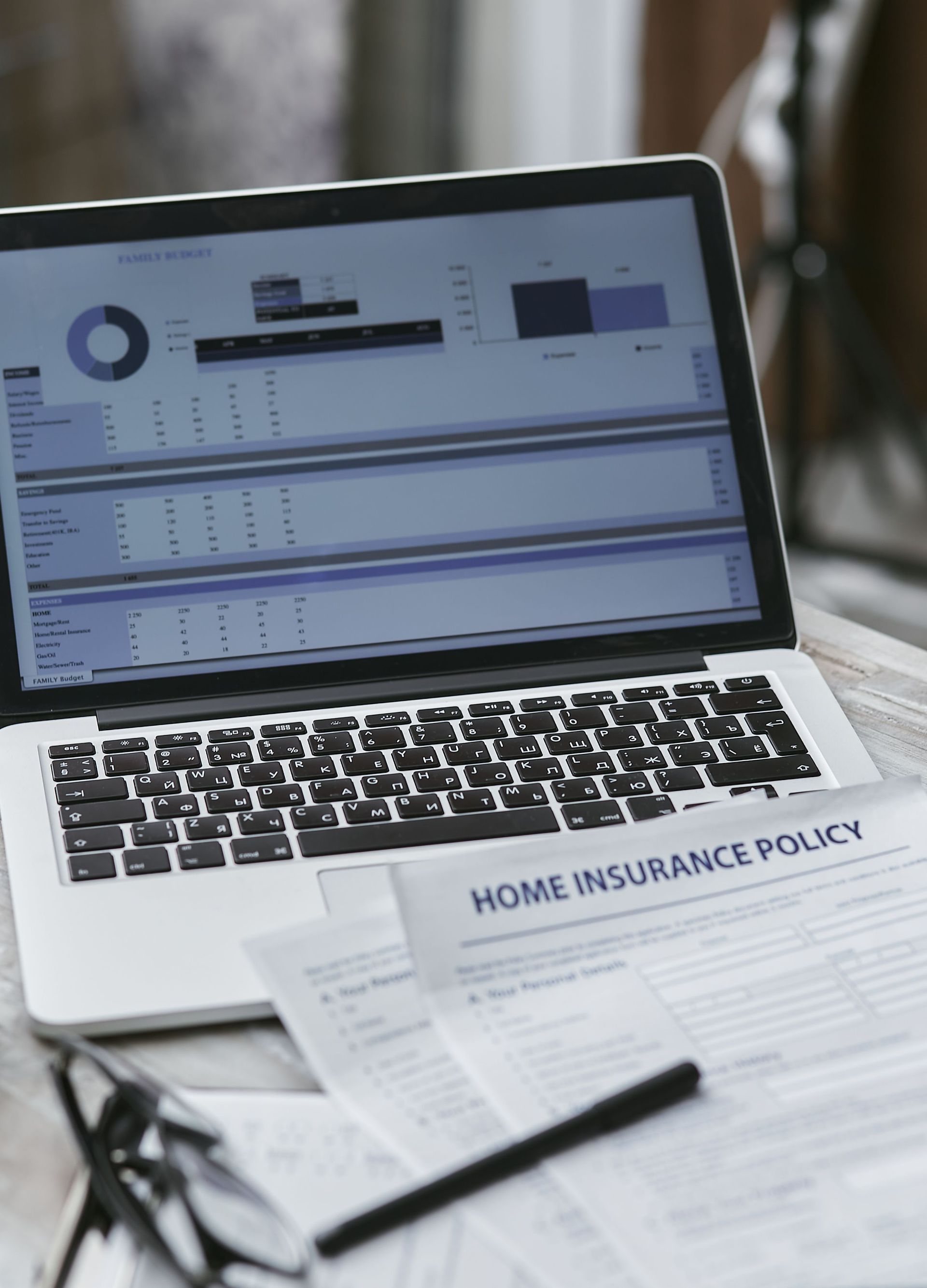Person in a suit holding a calculator over paperwork at a desk, with a laptop and house model nearby