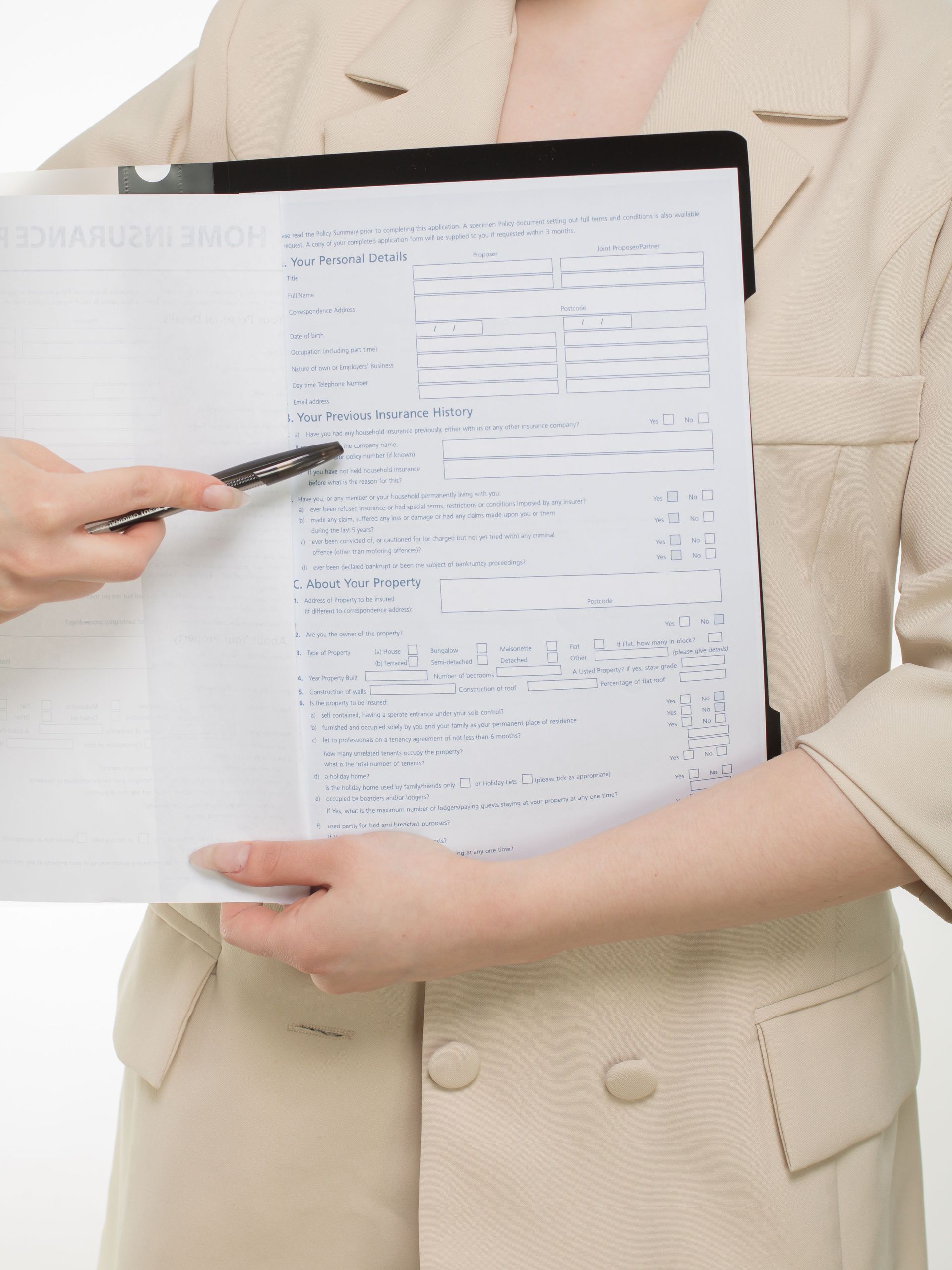 Hand filling out a paper bill beside a red notebook labeled “Pay” on a wooden desk