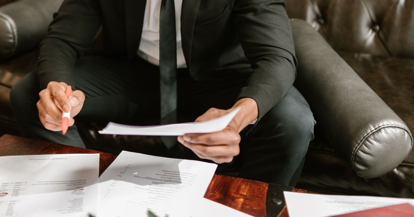 People in business attire signing documents, reviewing papers, and using a calculator at a desk.