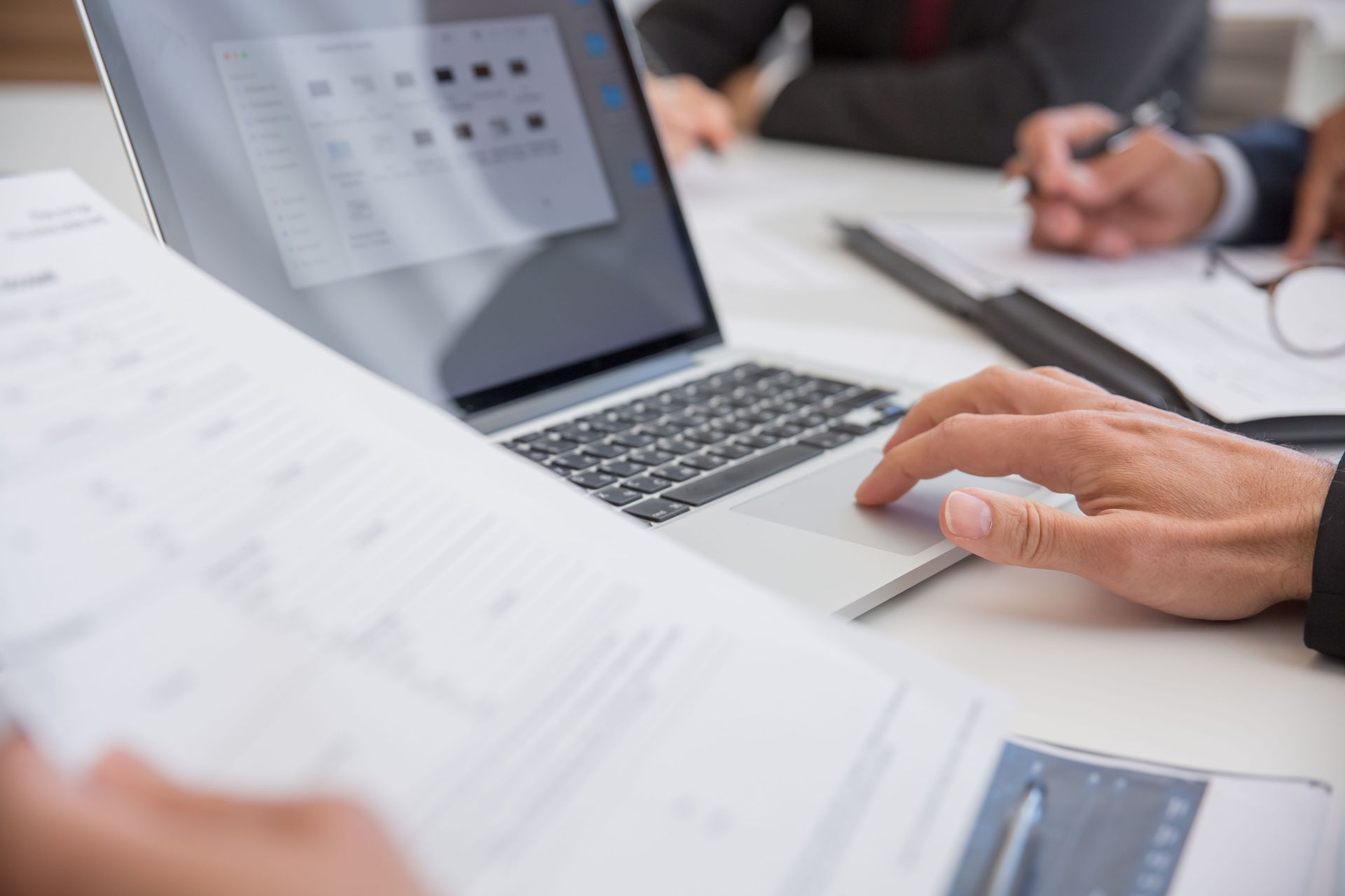 Business meeting with hands discussing documents, calculator, and laptop on a desk
