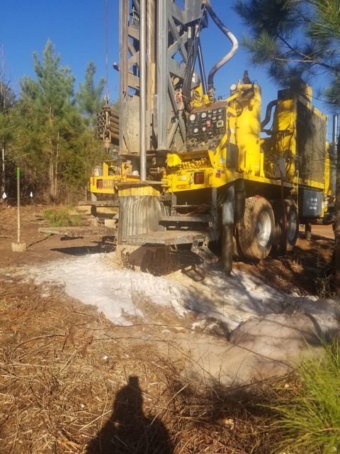 Yellow drilling rig spraying foam on dry ground in a wooded outdoor area