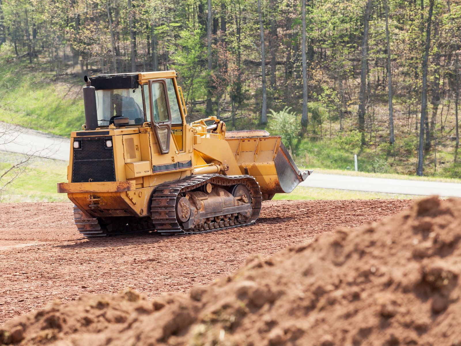Yellow bulldozer on brown earth, near a paved road and trees.