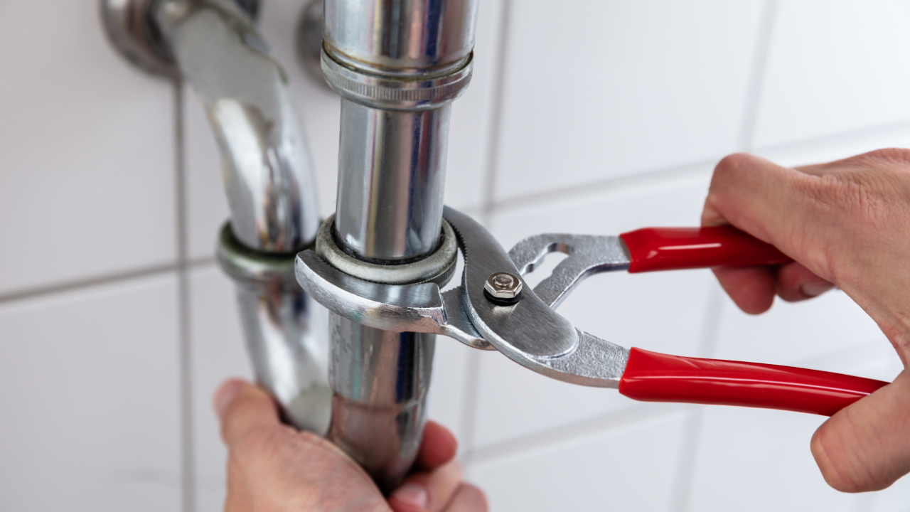 Plumber using pliers to tighten a pipe fitting in a bathroom.
