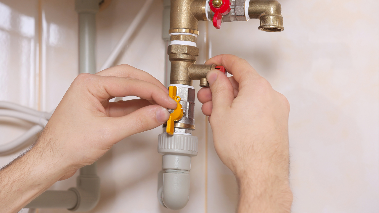 Hands turning valves on a plumbing system with brass pipes and white wall.