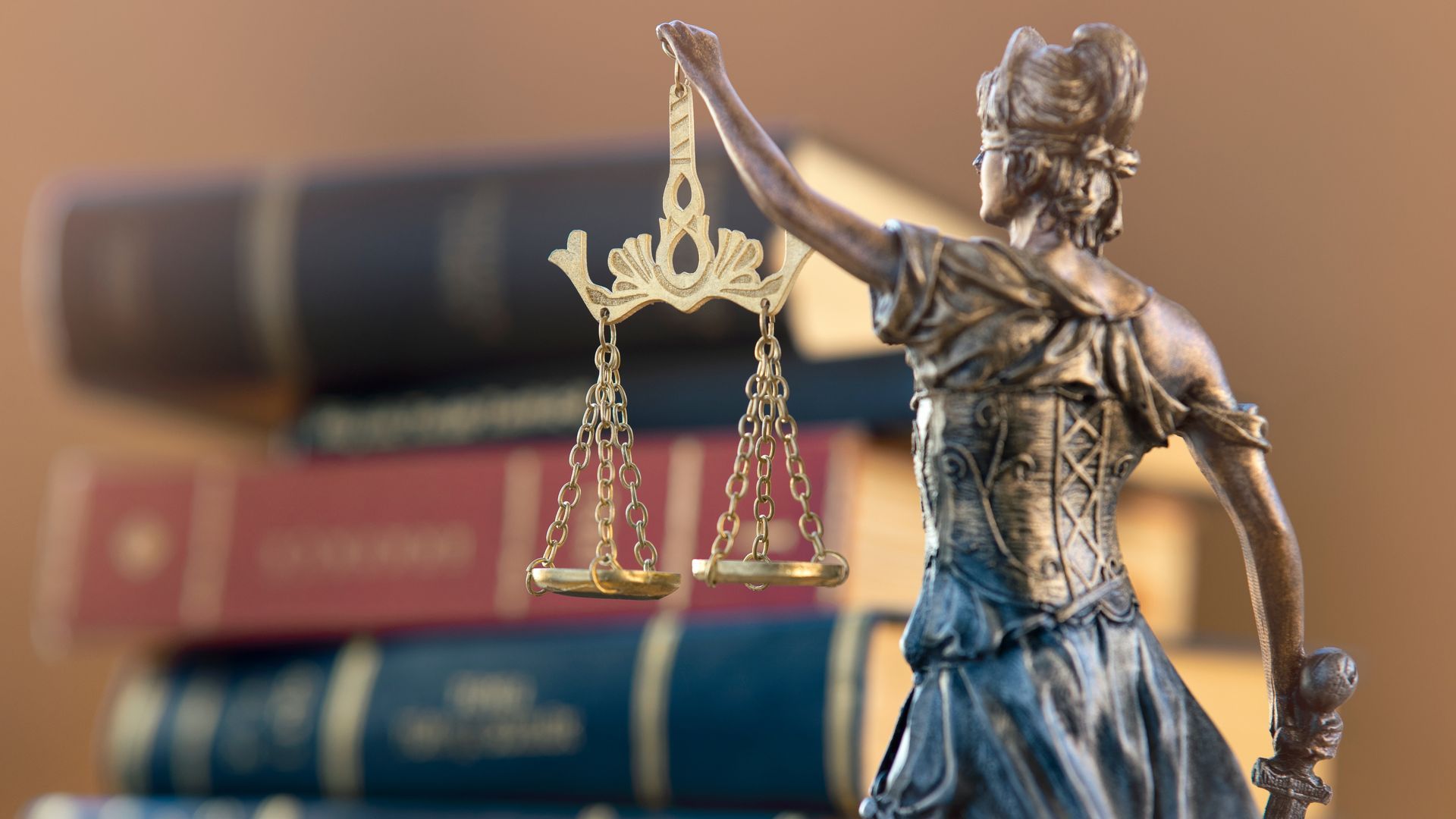 Statue of Lady Justice holding scales, in front of a stack of law books.
