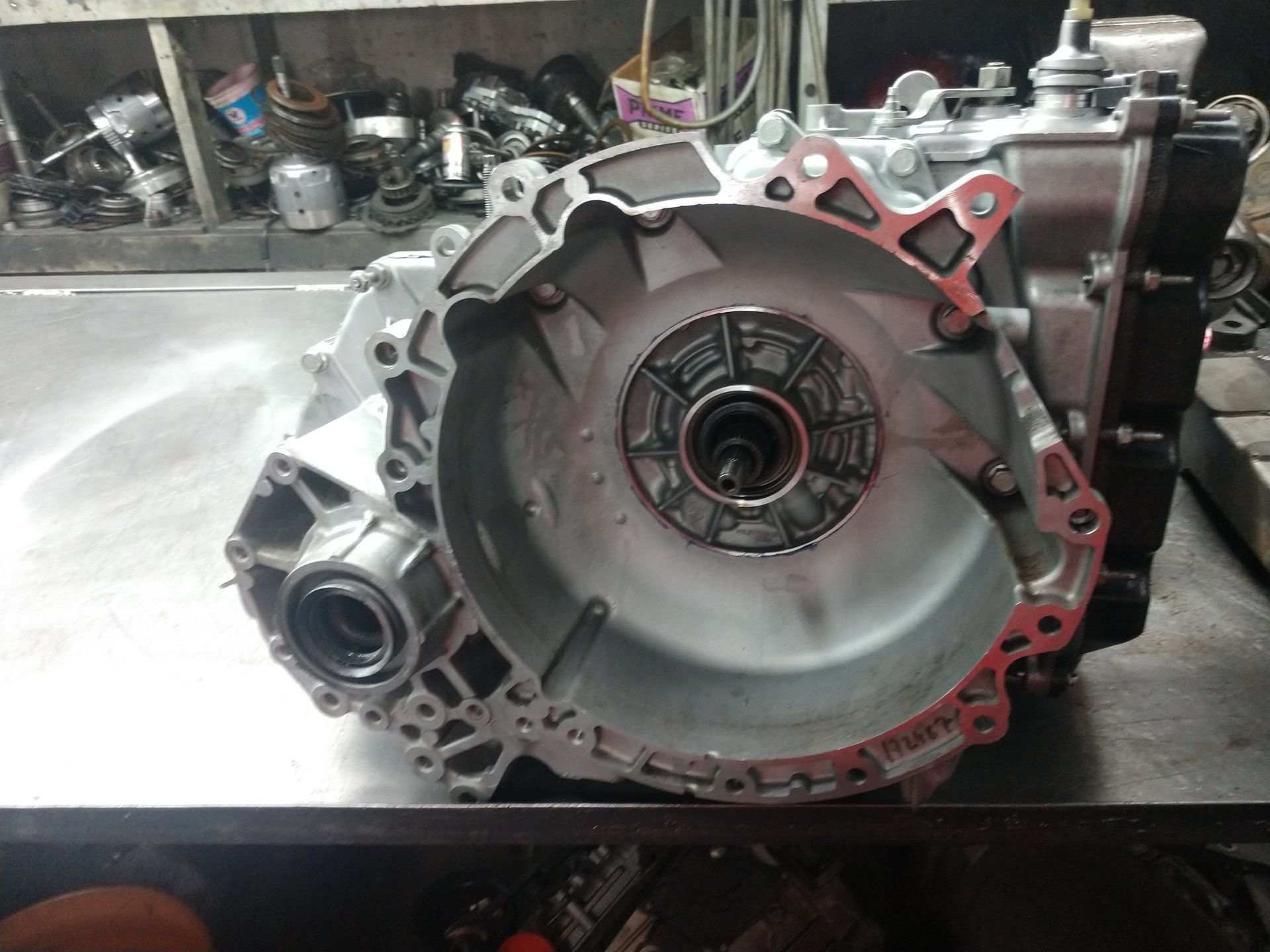 Close-up of a metal car transmission housing on a workshop table, with red gasket seal visible