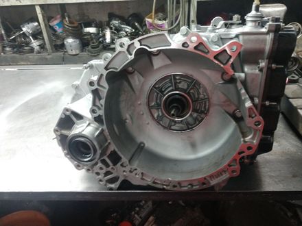 Close-up of a metal car transmission housing on a workshop table, with red gasket seal visible