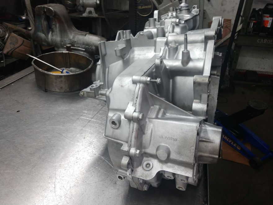 Silver transmission or gearbox housing on a workshop floor with a metal parts tray nearby