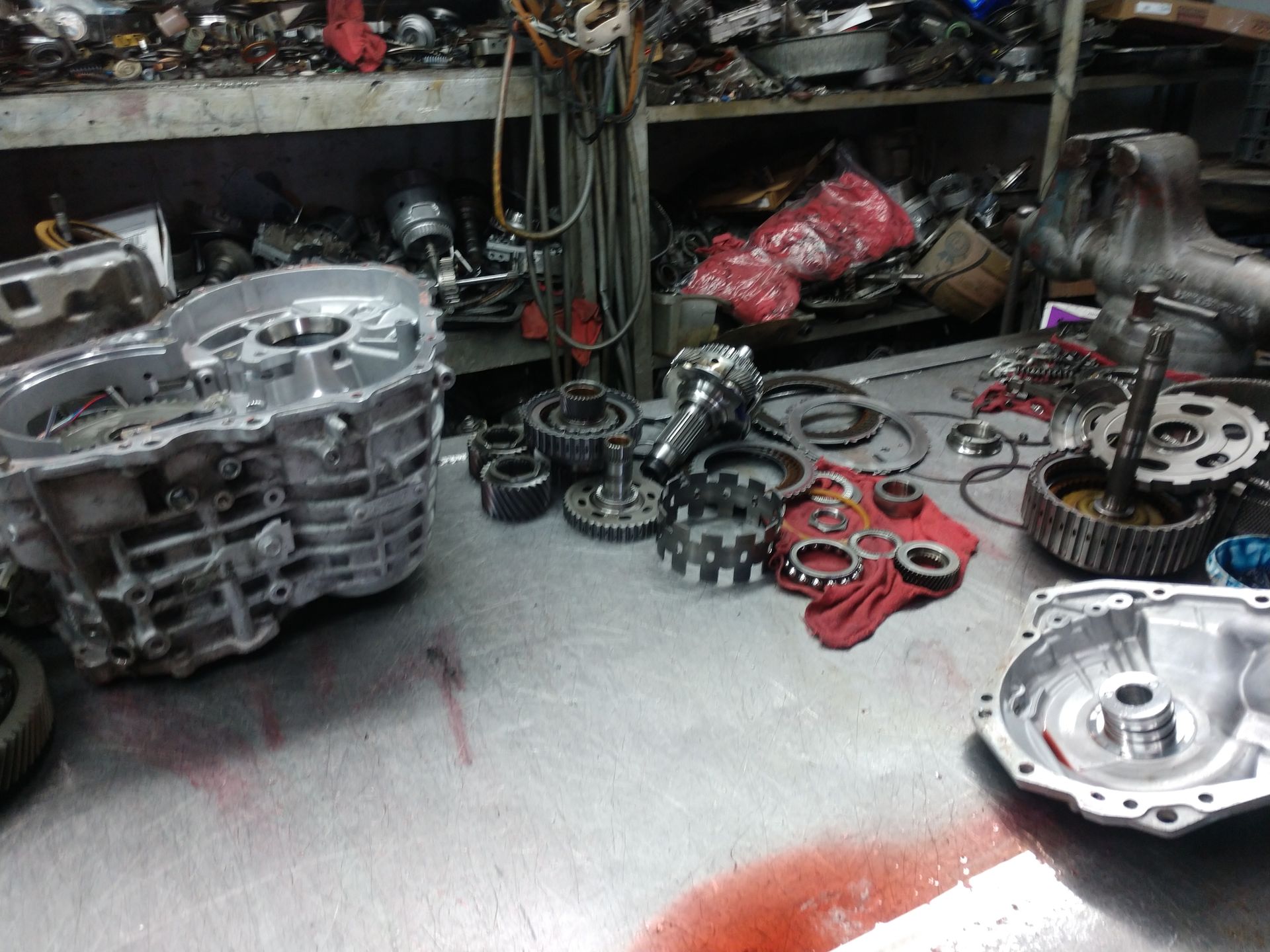 Auto parts and transmission components scattered across a workshop floor and shelves