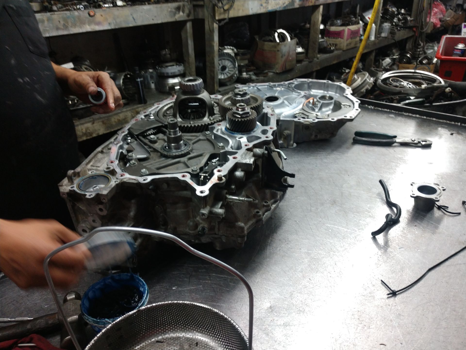 Mechanic working on an open car transmission in a cluttered auto repair shop