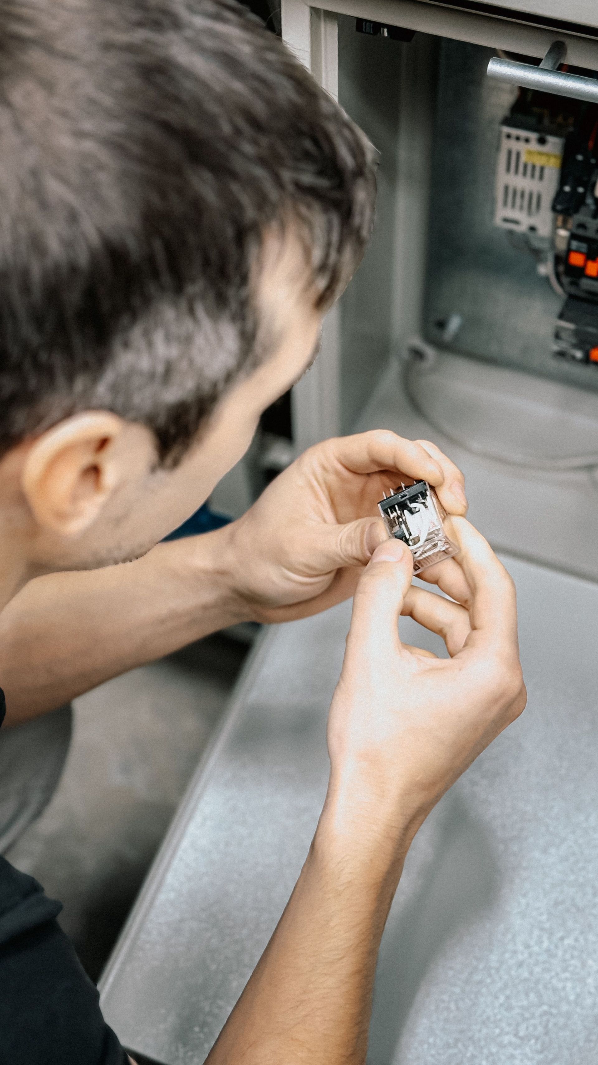 Person inspecting a small component inside an open electrical panel.