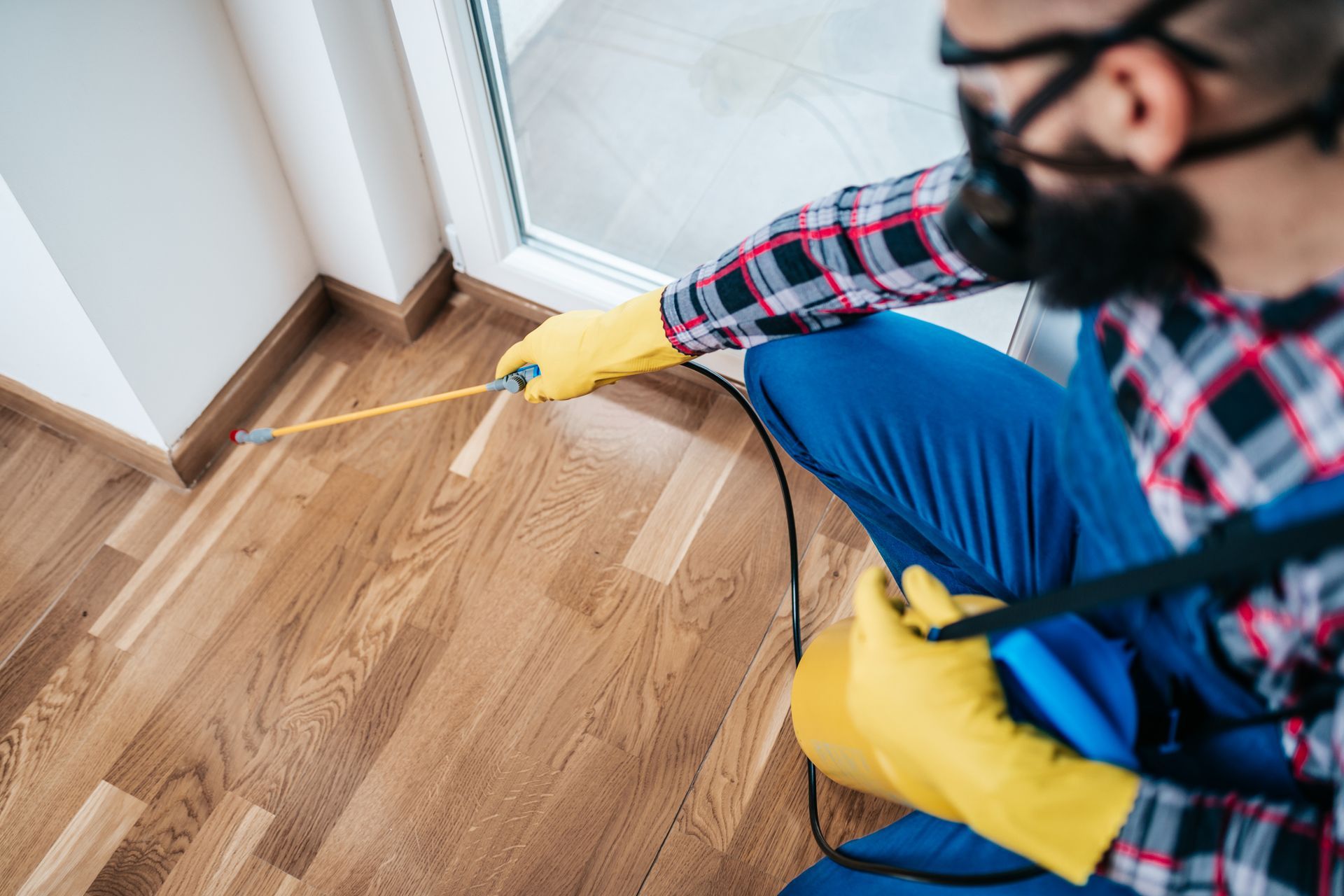An exterminator, from a pest control company, in protective workwear, is spraying pesticide indoors.