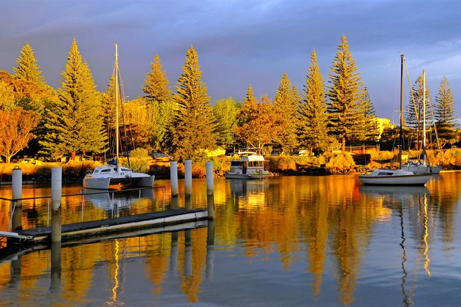 Sunset over calm water with sailboats; orange and yellow sky reflected in the water.