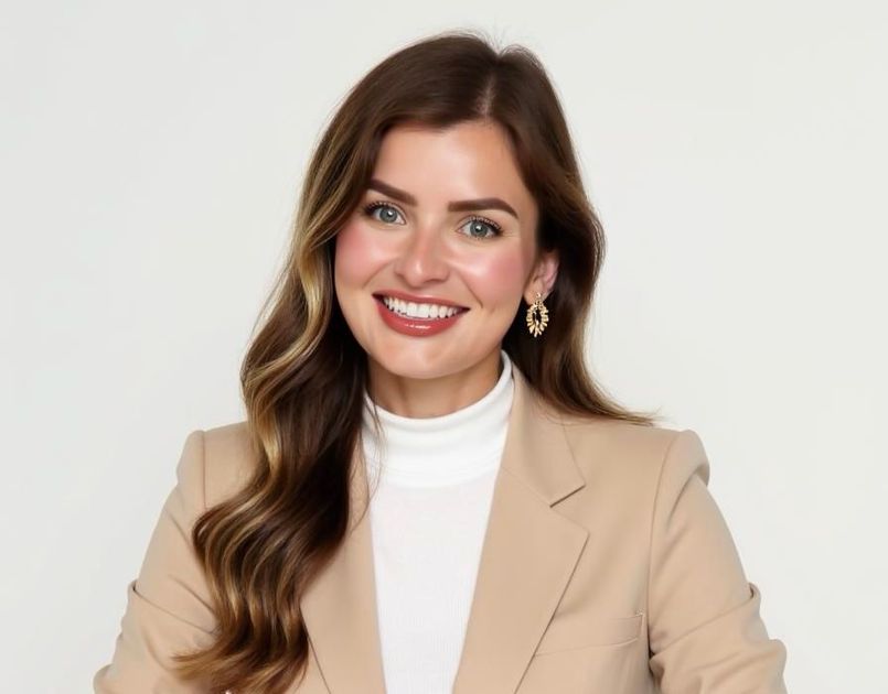 A professional headshot of a smiling woman with blonde hair, wearing a navy blue blazer and white shirt.
