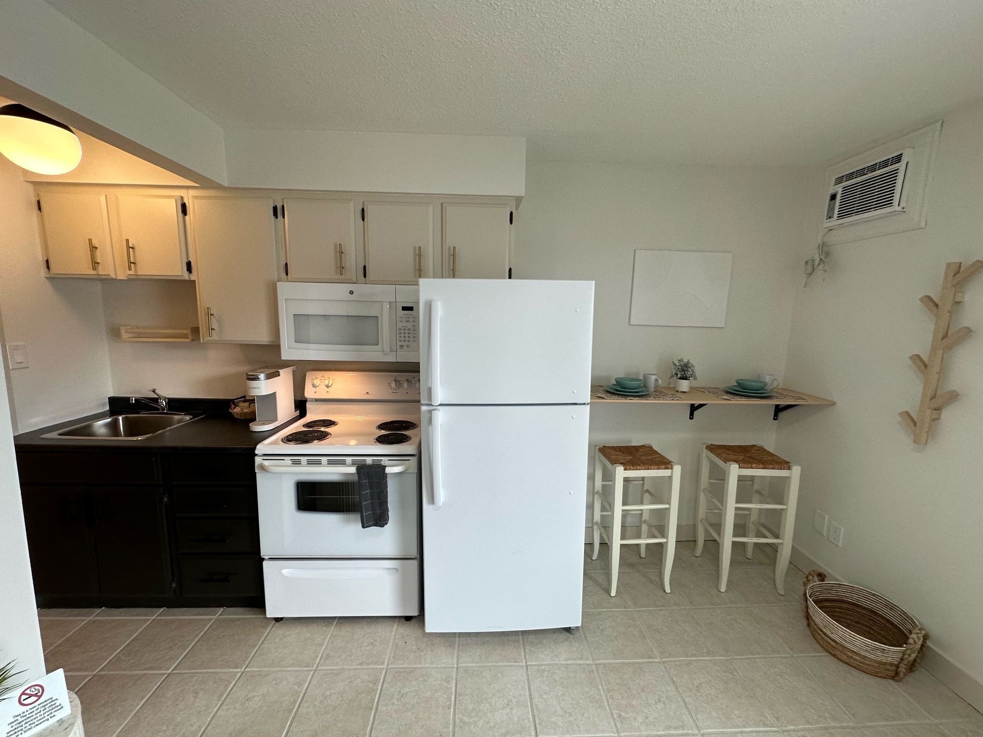 A white kitchen with dark cabinets, white appliances, a small breakfast bar with two wooden stools, and a pet bed.