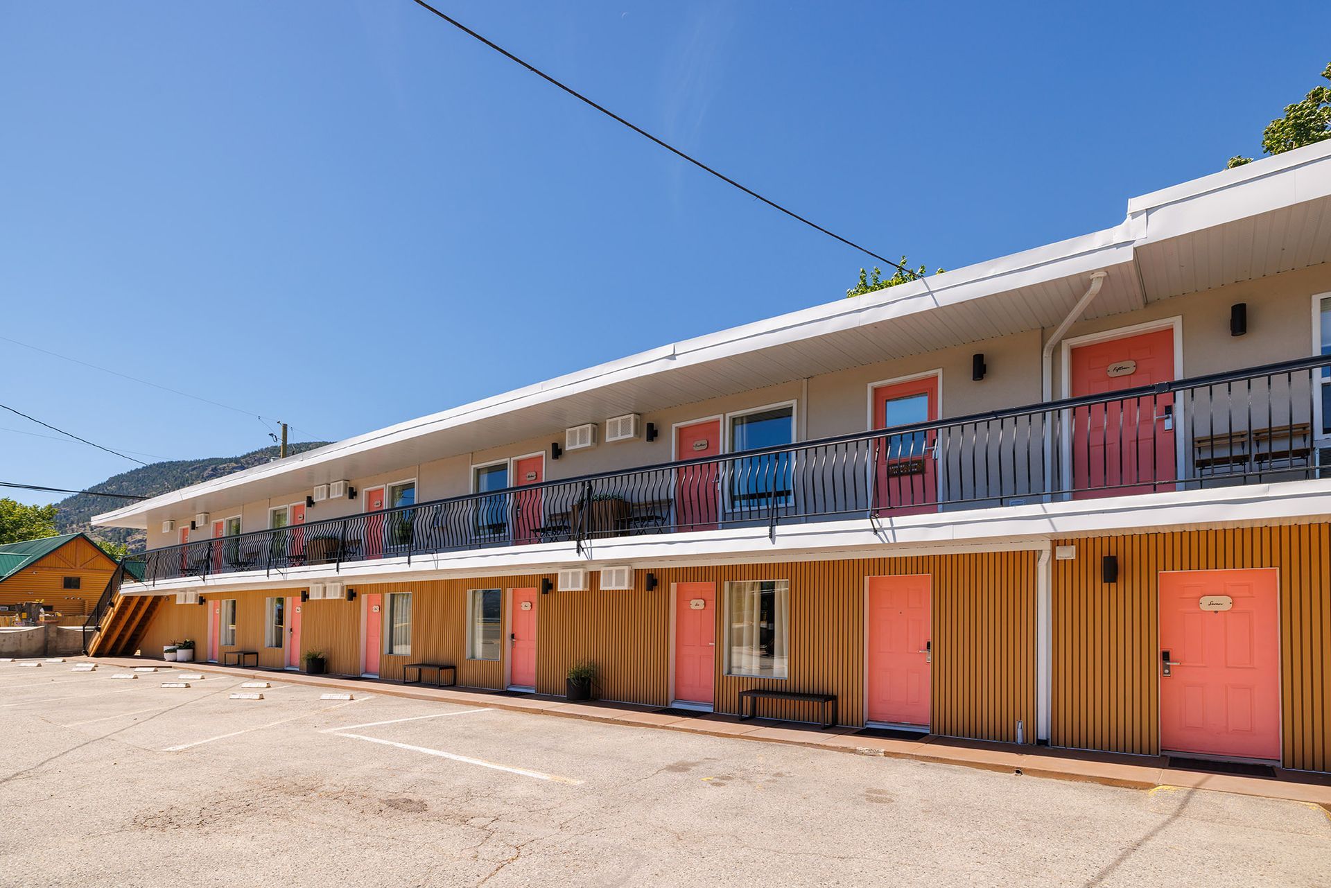 Two-story motel with pink doors, light gray siding, blue trim, and a black metal railing along the upper walkway.