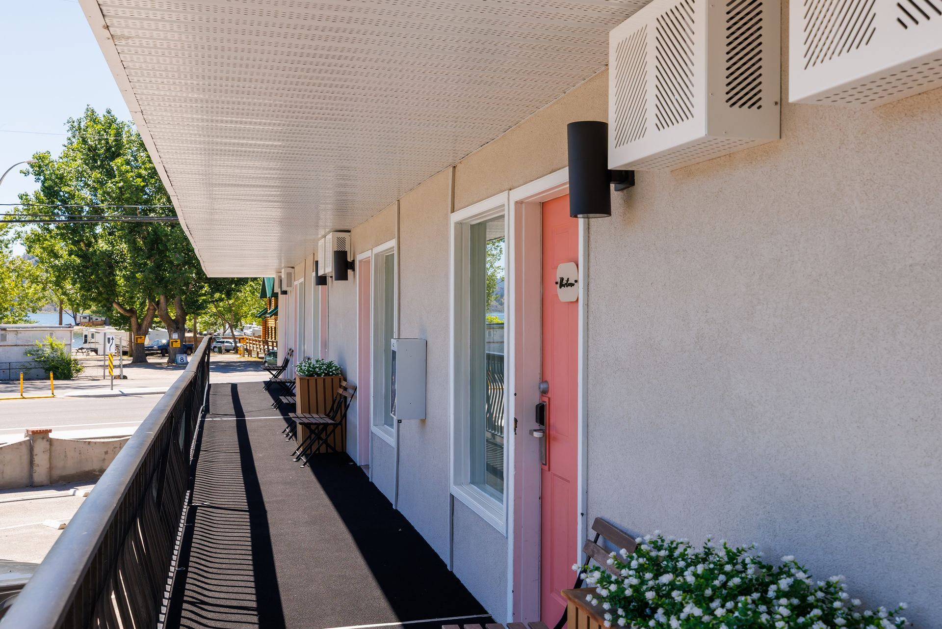 A low-angle view of a motel exterior with vertical tan siding, a long walkway, and outdoor benches under a porch overhang.