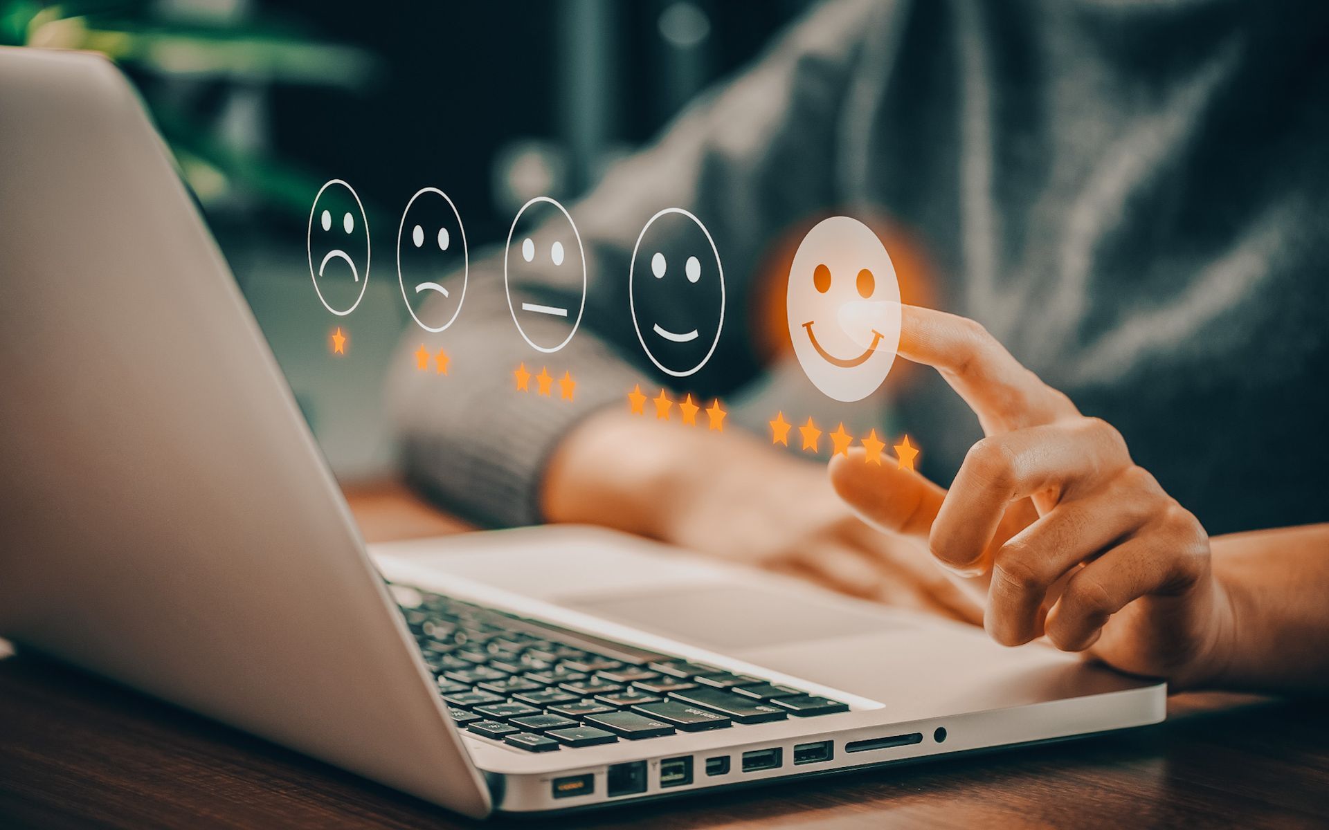 A person uses a finger to select the positive smiley face icon on a laptop screen to give a five-star rating.