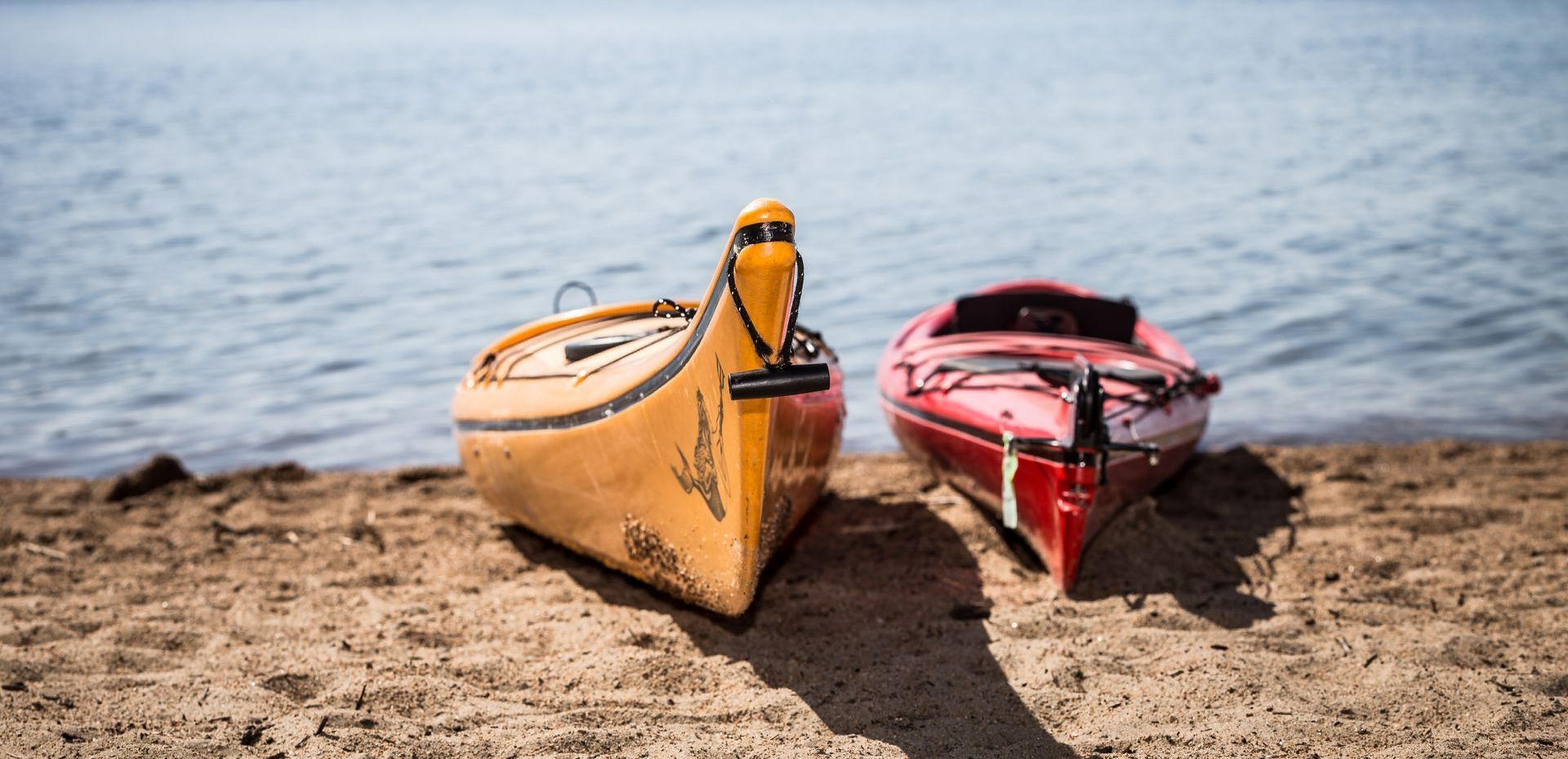 A yellow canoe and a red kayak rest side-by-side on a sandy lakeshore.