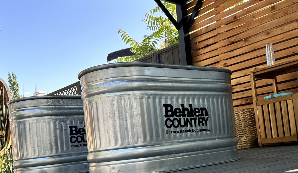 Two Behlen Country galvanized steel stock tanks sitting on a deck next to a wooden fence.