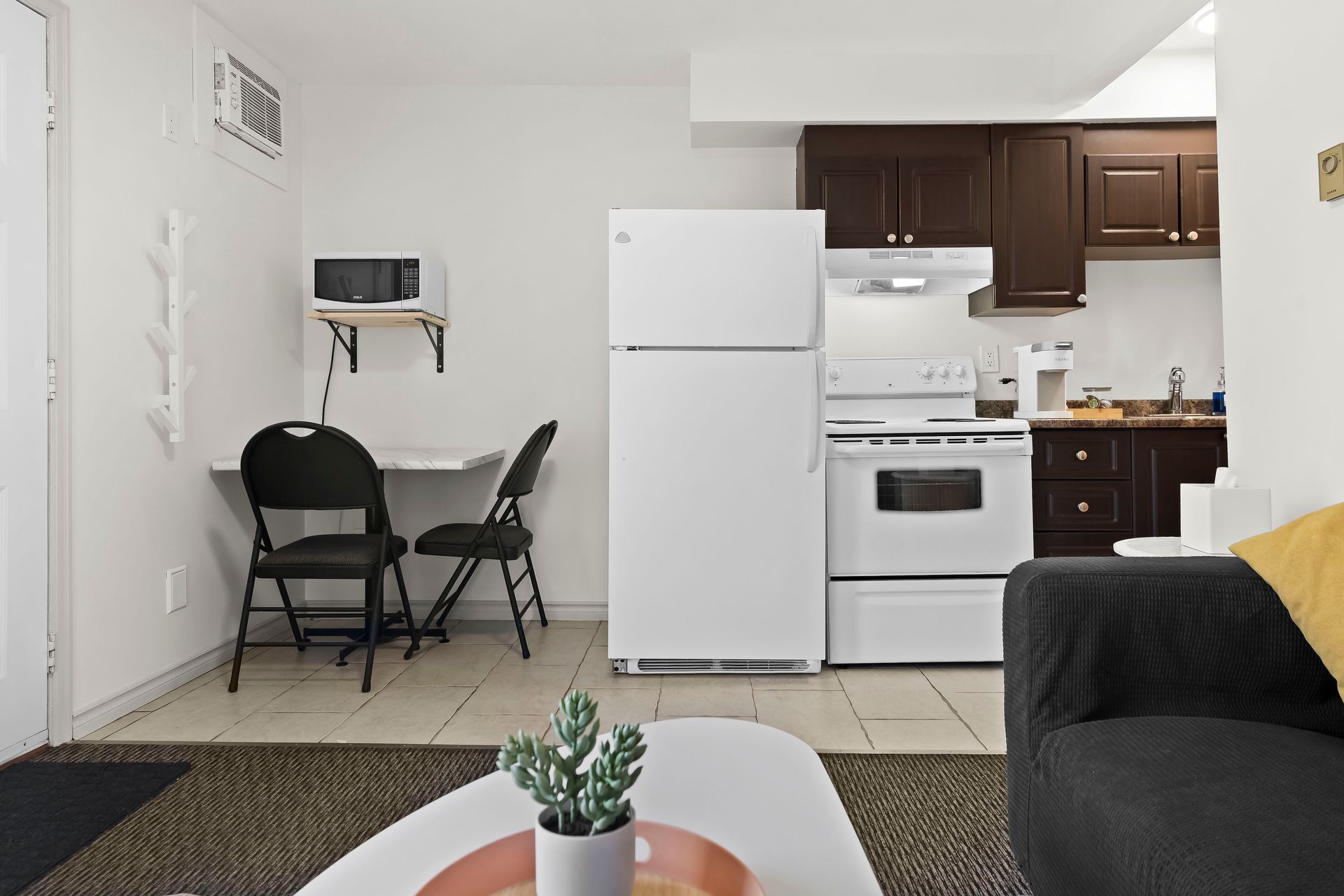A compact kitchen area featuring a white refrigerator and stove, a wall-mounted microwave, and a small dining table.