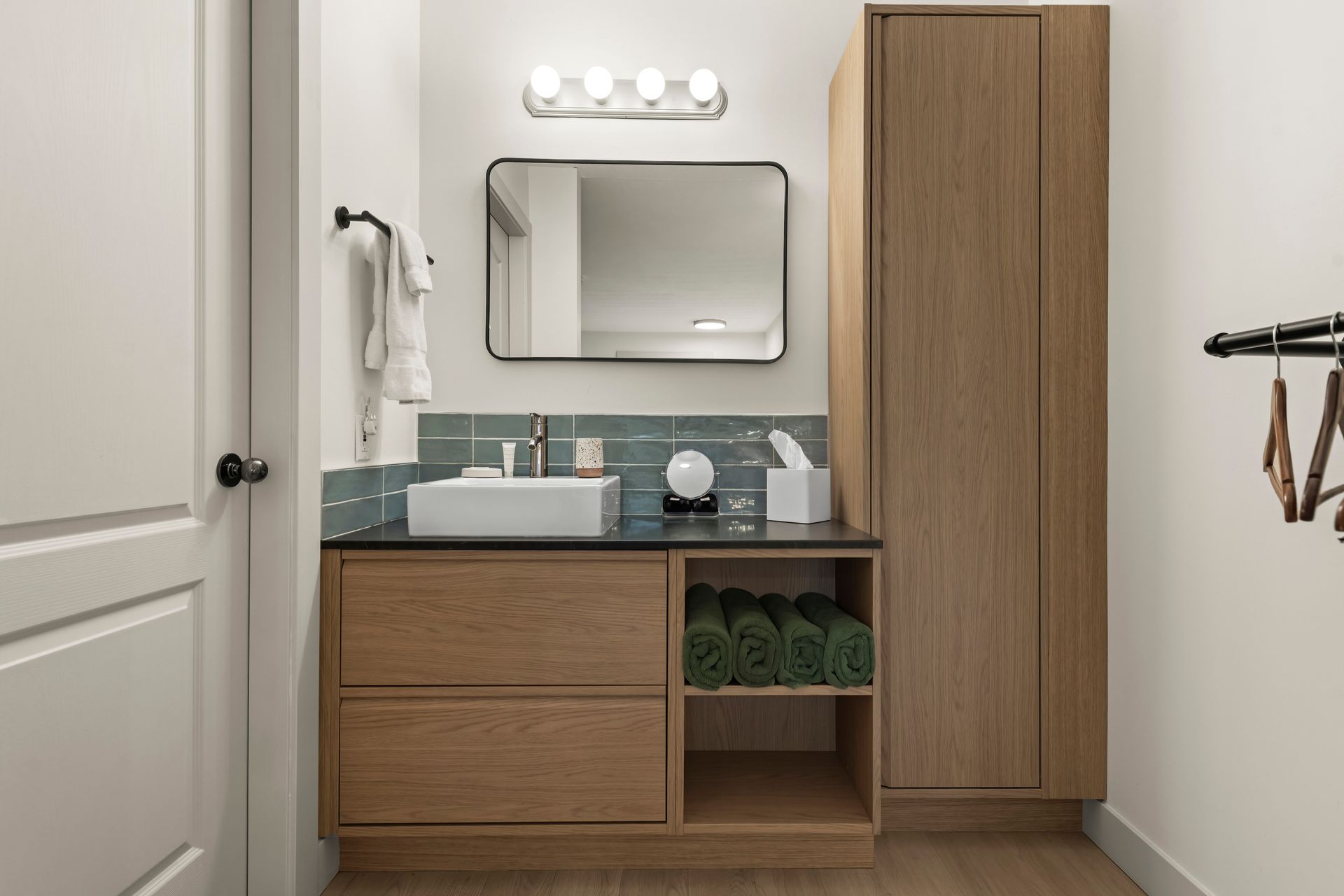 Modern bathroom vanity with a white vessel sink, wooden cabinet, blue tile backsplash, and mirror on a plain wall.