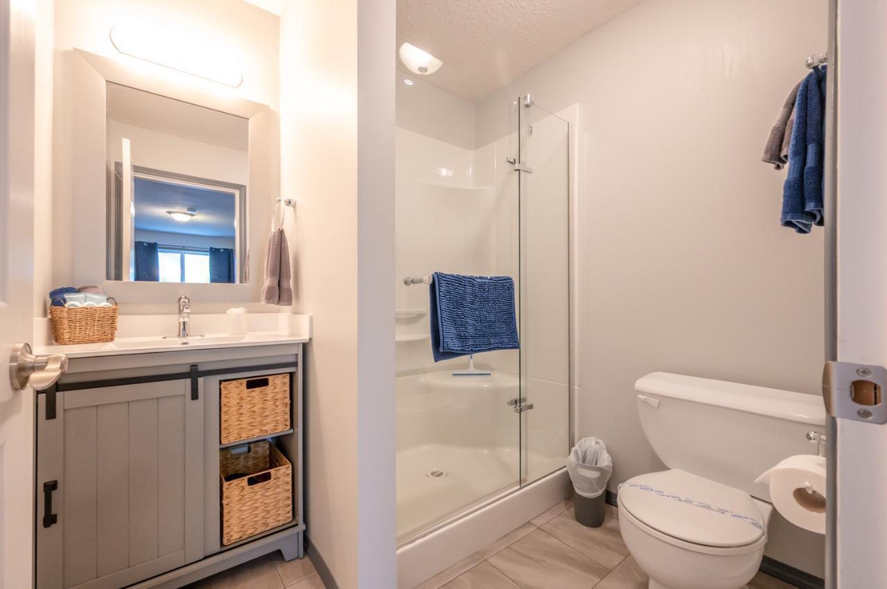 Modern bathroom with a gray vanity, woven baskets, a glass shower stall, and a white toilet.