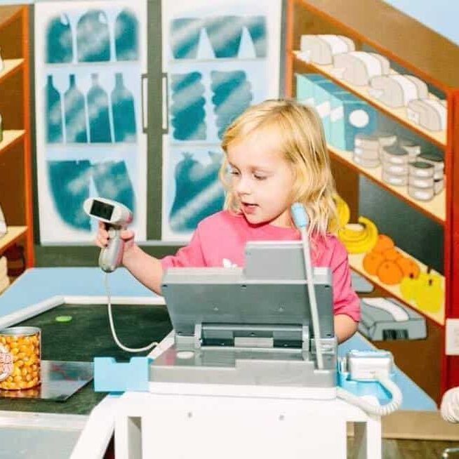A little girl is playing with a cash register in a store
