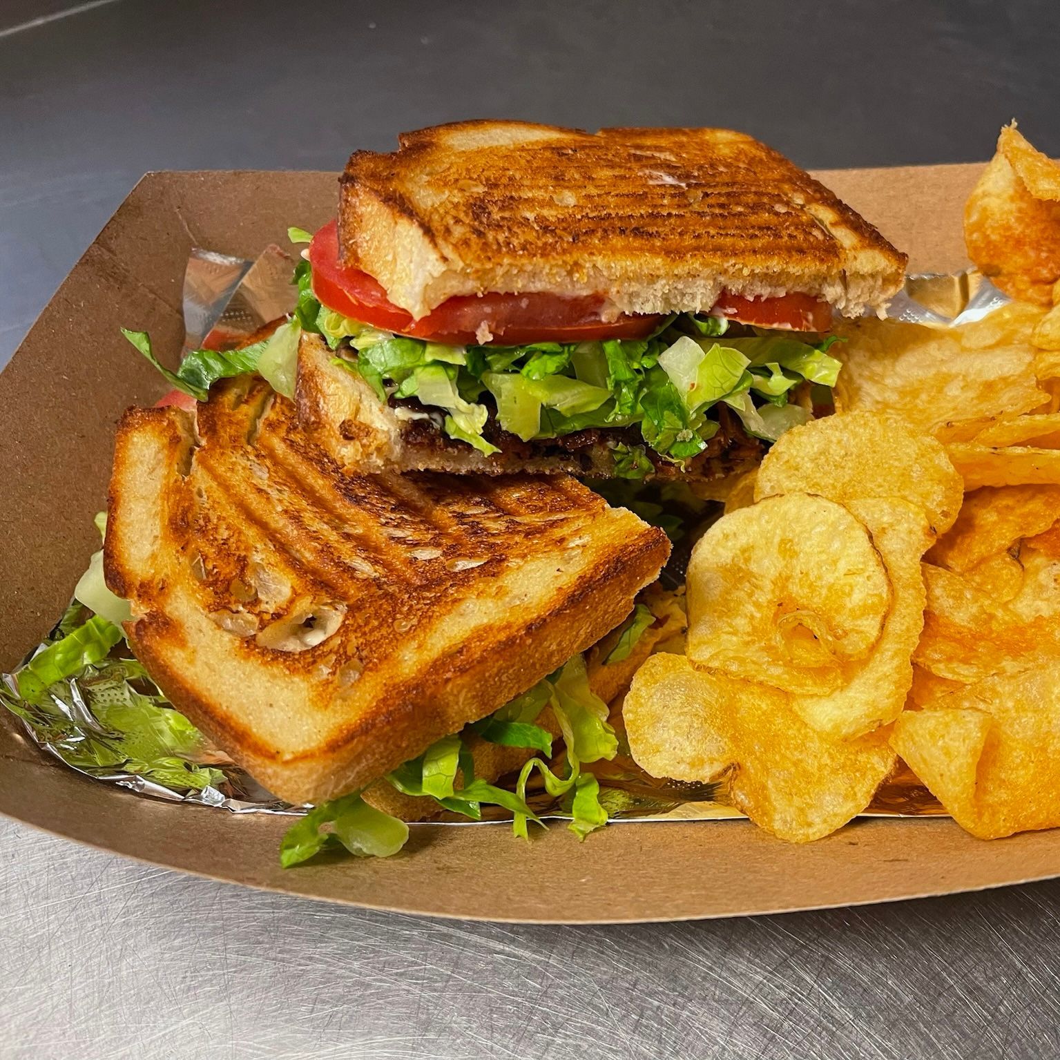 A grilled cheese sandwich and potato chips on a paper plate.