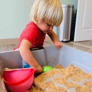 A little boy is playing in a sandbox with a bucket and shovel.