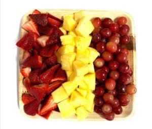 A wooden tray filled with strawberries , pineapple and grapes.