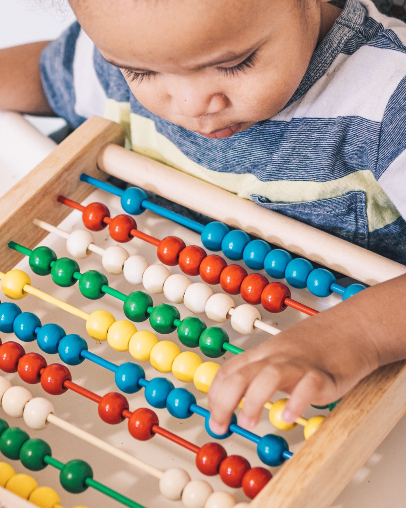 A young boy is playing with a wooden abacus.