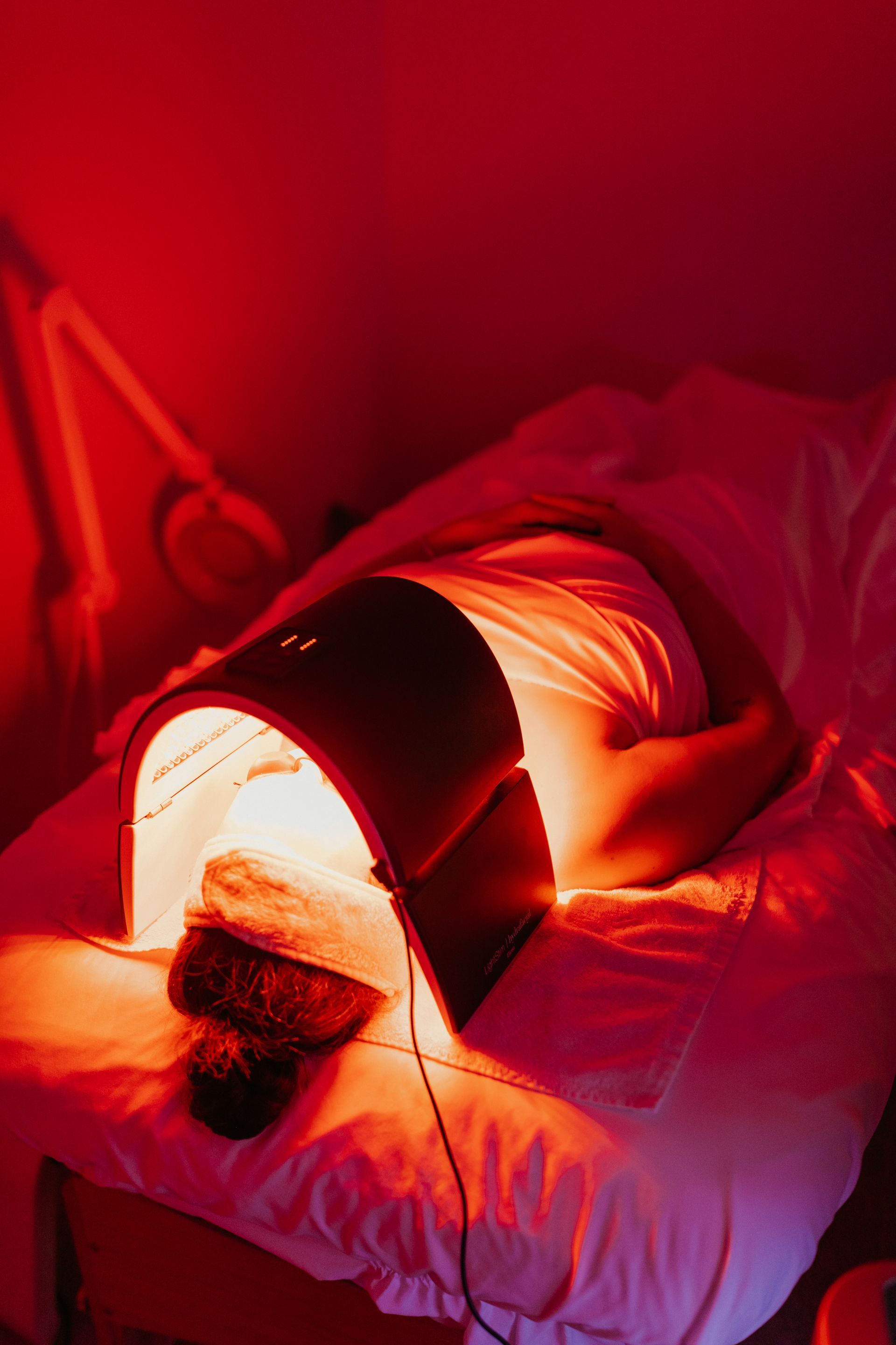 Person receiving red light therapy treatment, lying on a bed with light-emitting device over face.