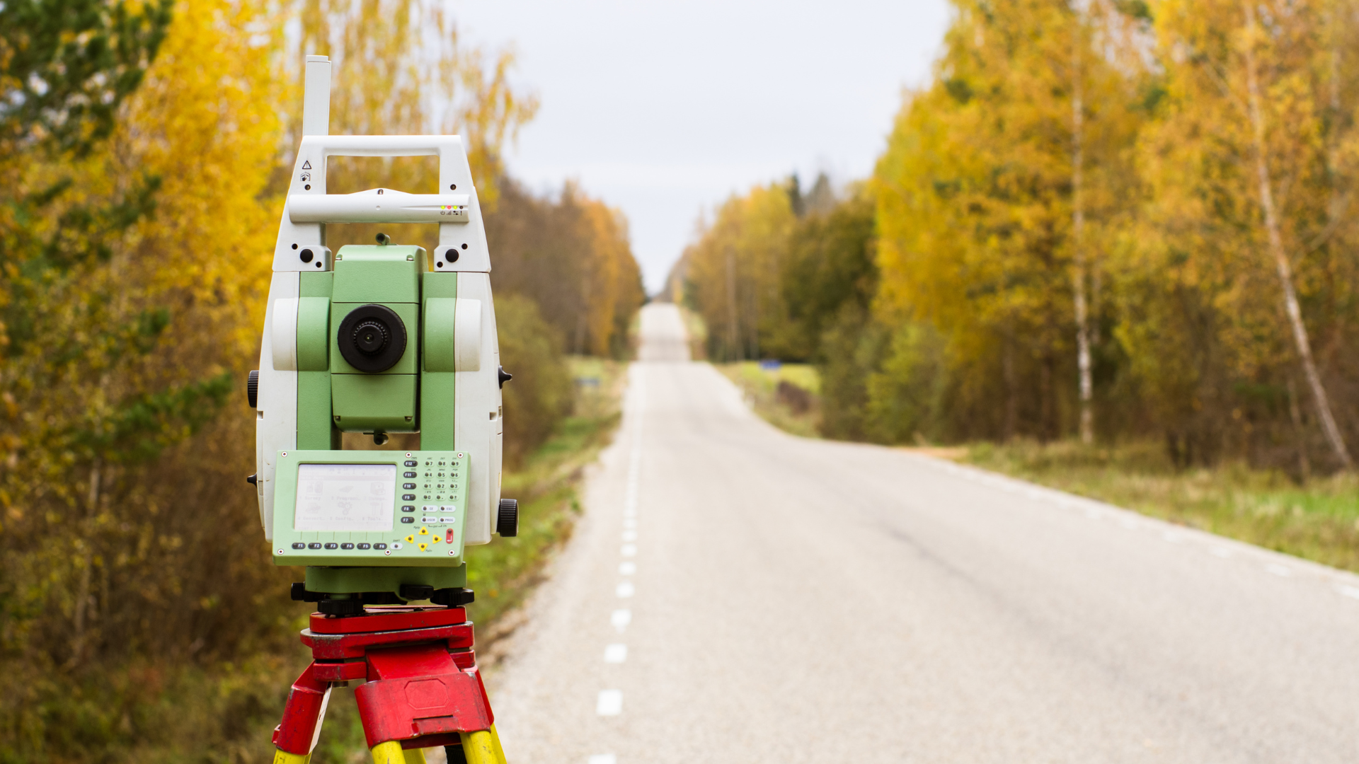 A theodolite is sitting on a tripod on the side of a road.