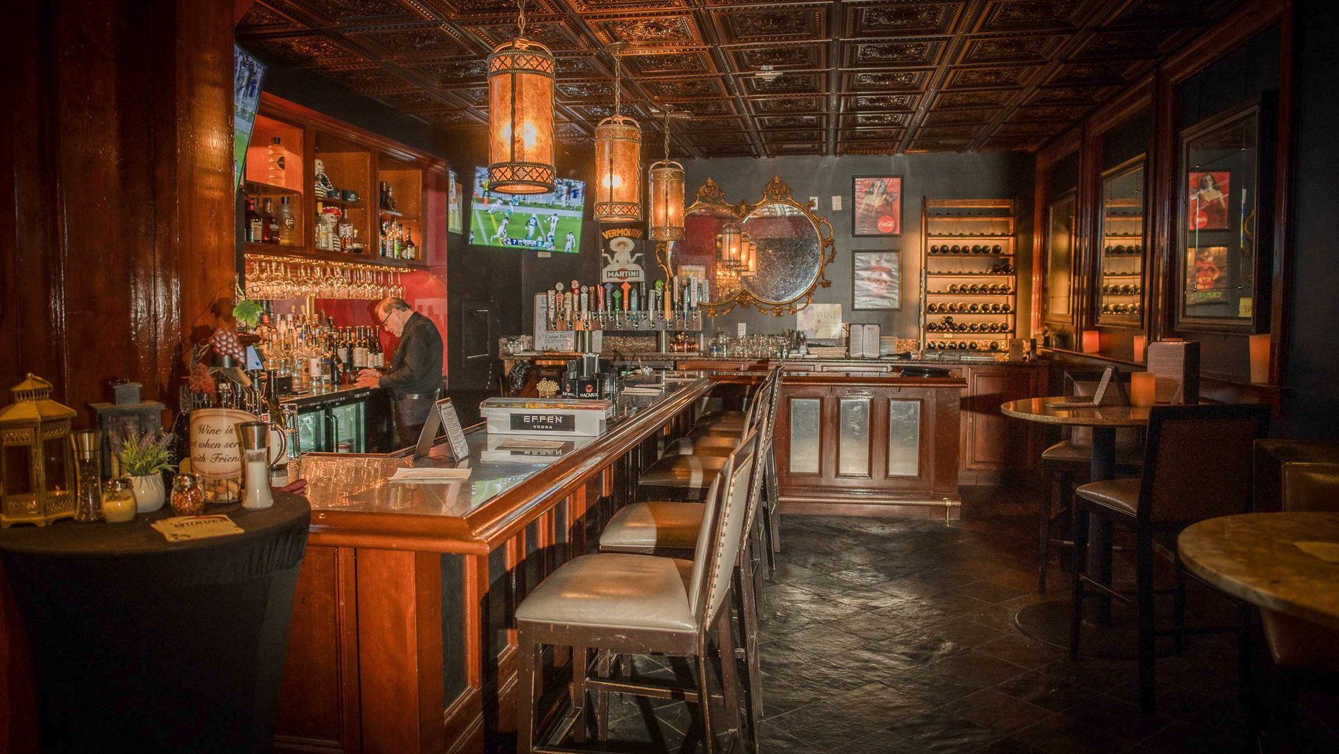 Interior of a dimly lit bar with a long wooden bar, stools, and ornate ceiling fixtures.