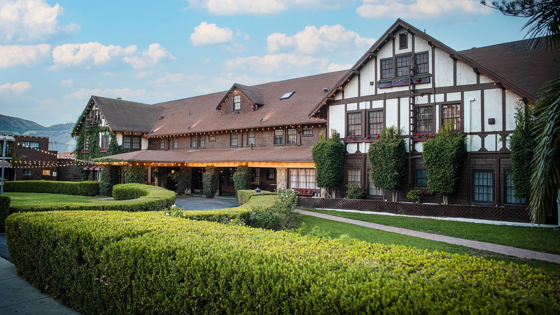 Tudor-style building with brown timbers and white stucco, surrounded by a green lawn and hedges.
