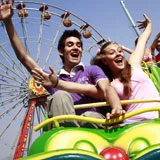 People on a roller coaster ride at an amusement park with a Ferris wheel in the background.