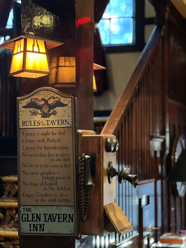 Sign for Rules Tavern with list of rules, antique phone, and a staircase.