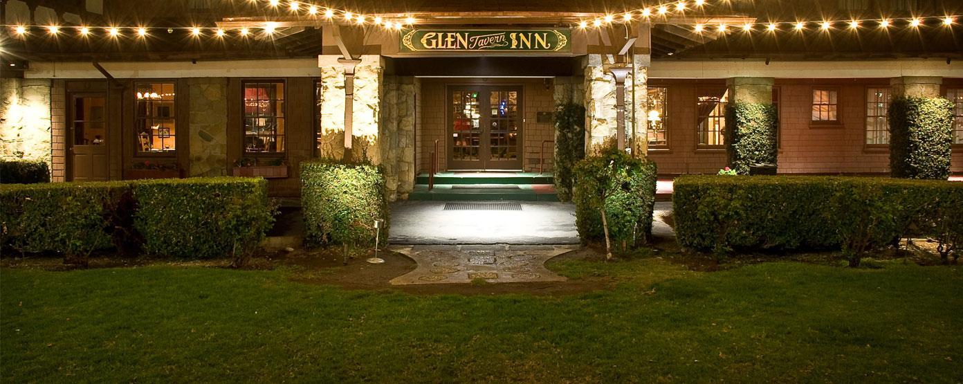 Night view of the Columbo Inn's entrance, lit with string lights and garden hedges.