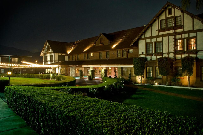 A Tudor-style hotel illuminated at night, with manicured hedges and a green lawn.