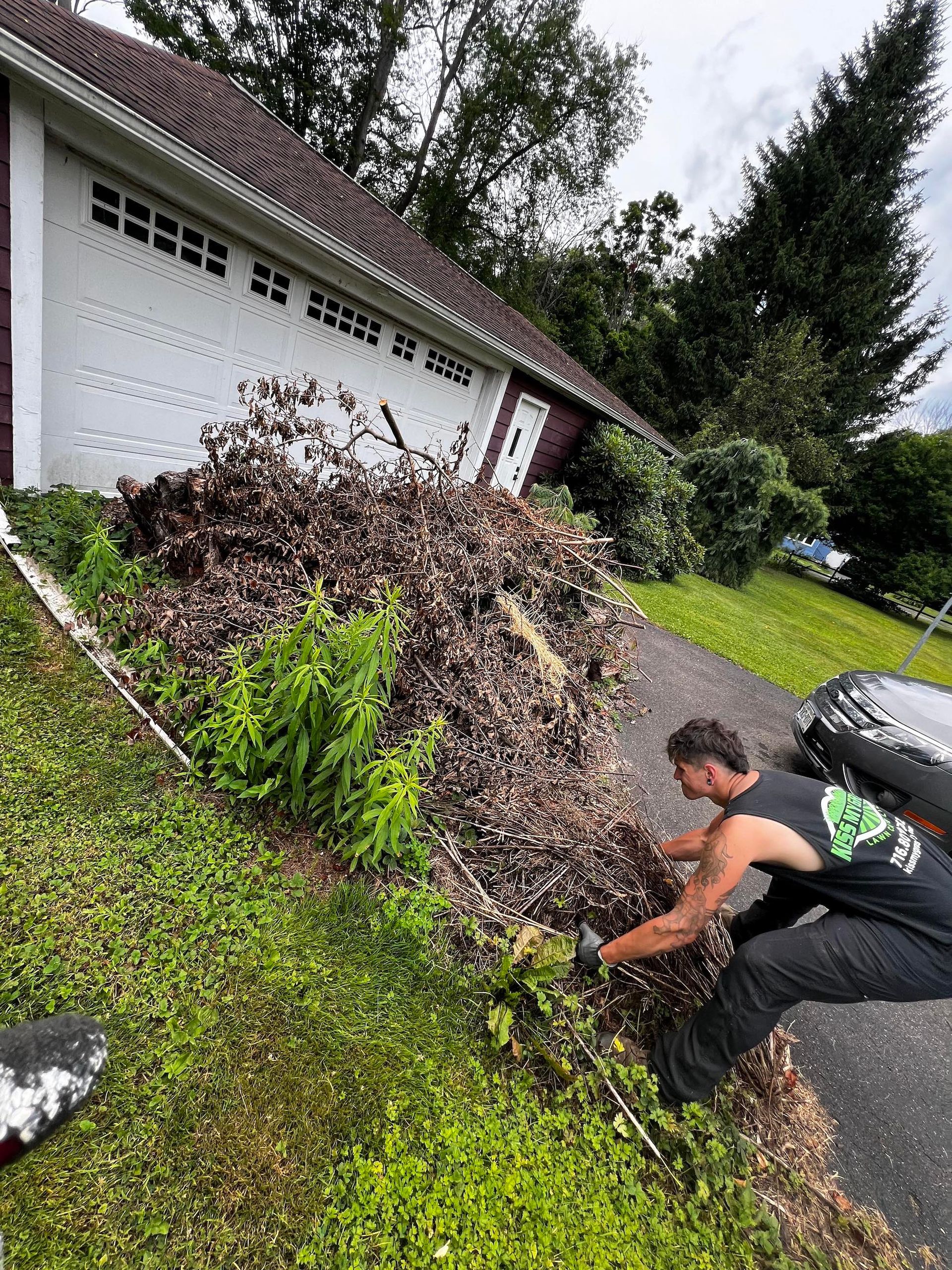 A man is kneeling down next to a pile of leaves in front of a garage.