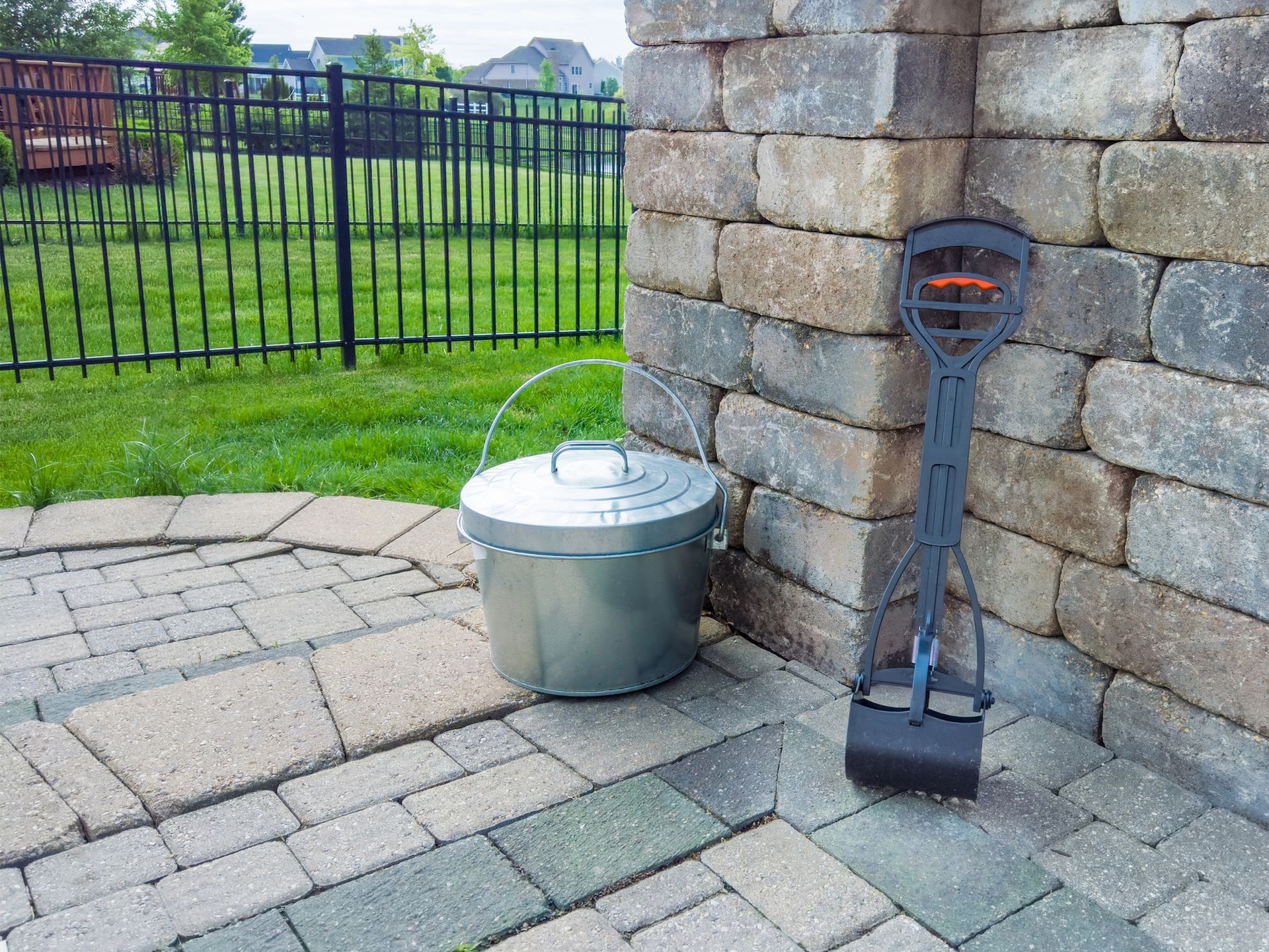 A metal bucket is sitting on a brick patio next to a brick wall.
