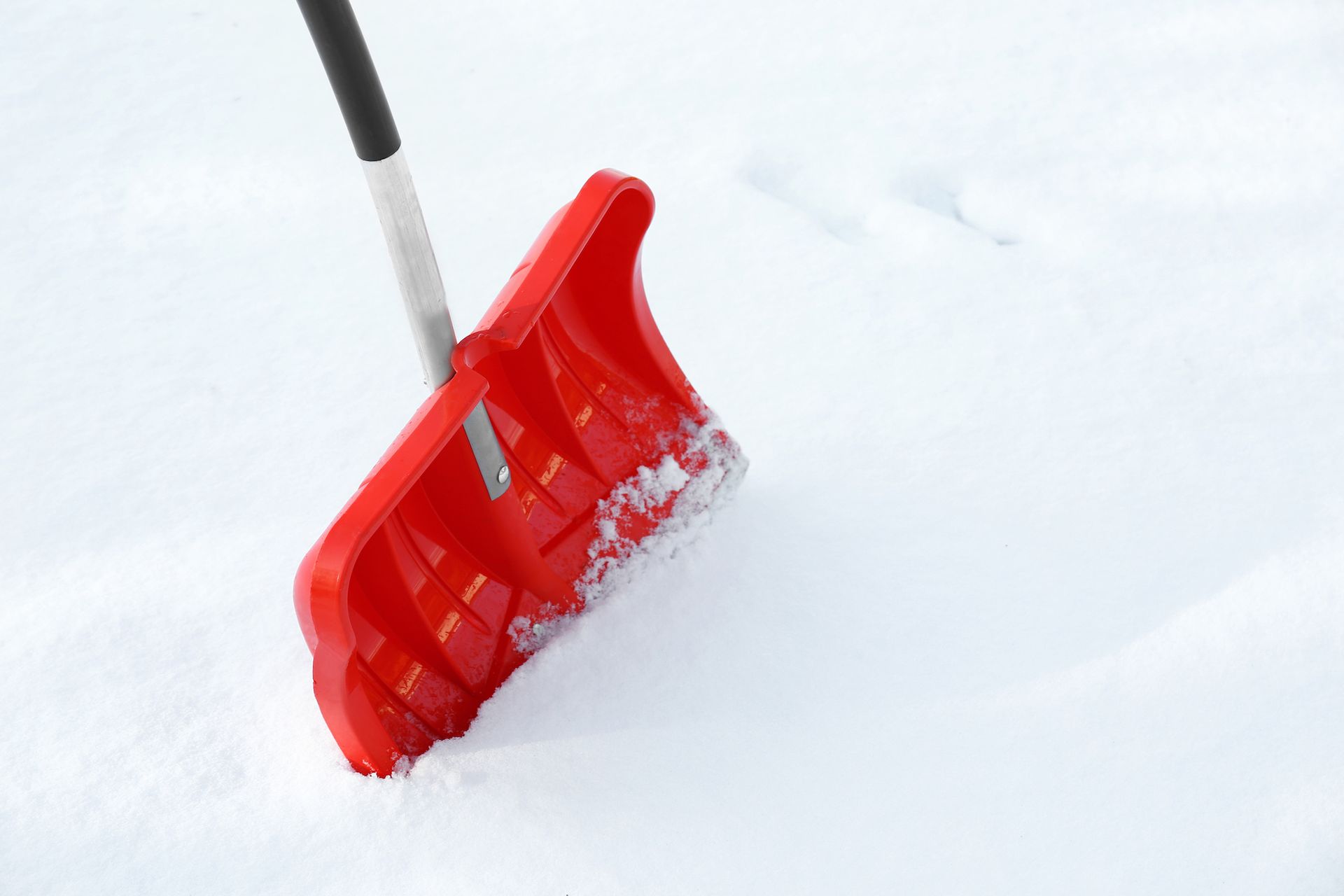 A red snow shovel is sitting in the snow.