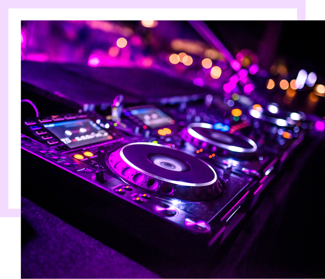 Table de mixage DJ illuminée en violet, décor avec lumières floues en arrière-plan.