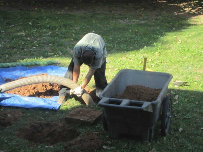 a man is working in the dirt next to a wheelbarrow filled with dirt .