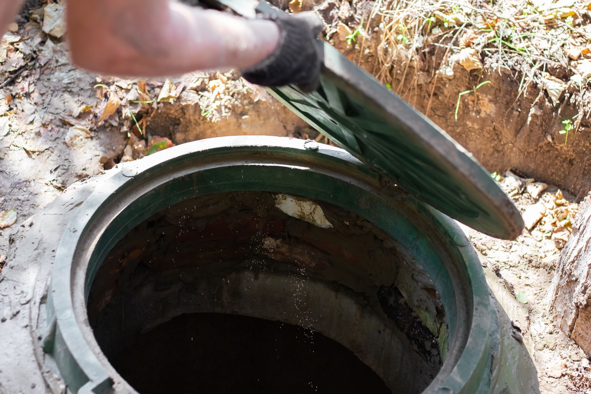 Person opening a green septic tank lid outdoors.