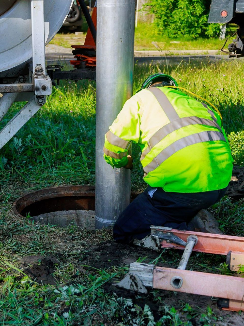 a man in a green jacket is kneeling down next to a manhole cover .