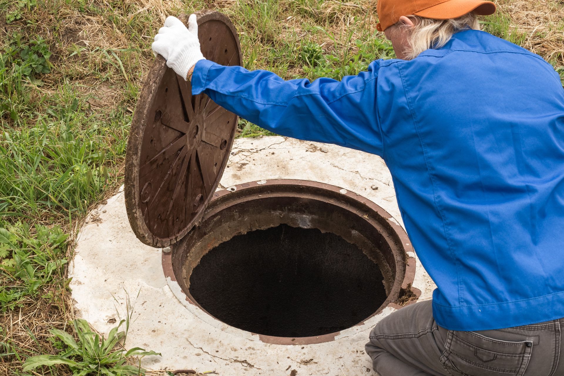 a man in a blue jacket is opening a manhole cover .