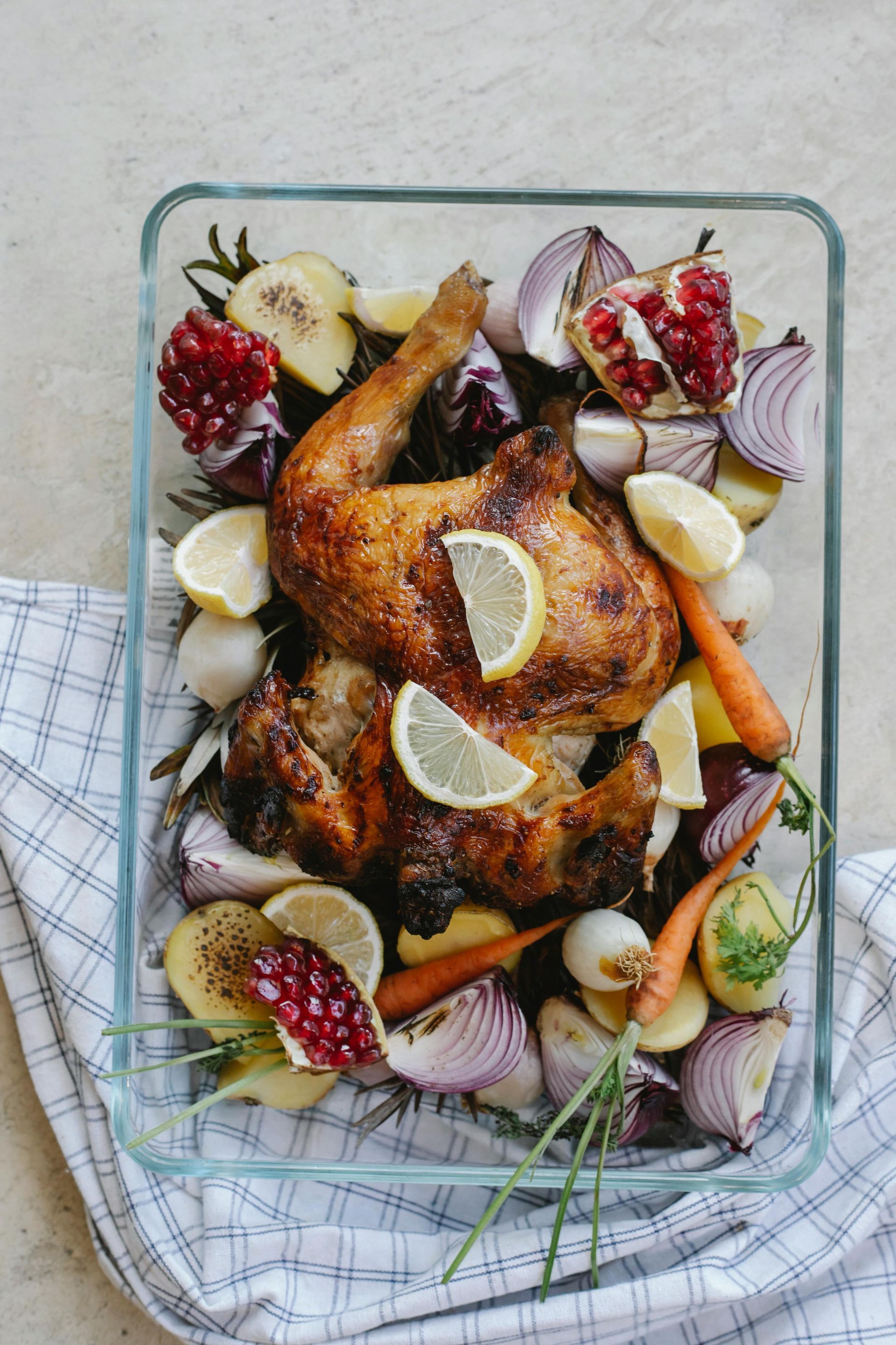 A roasted chicken surrounded by vegetables in a glass pan.